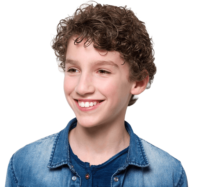 A young boy with curly brown hair and wearing a denim button-up shirt smiles as he gazes to his right
